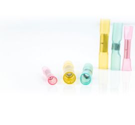 Two red, two yellow and two blue heat shrink butt connectors, insulated, three standing upright and three lying down, on a white background.